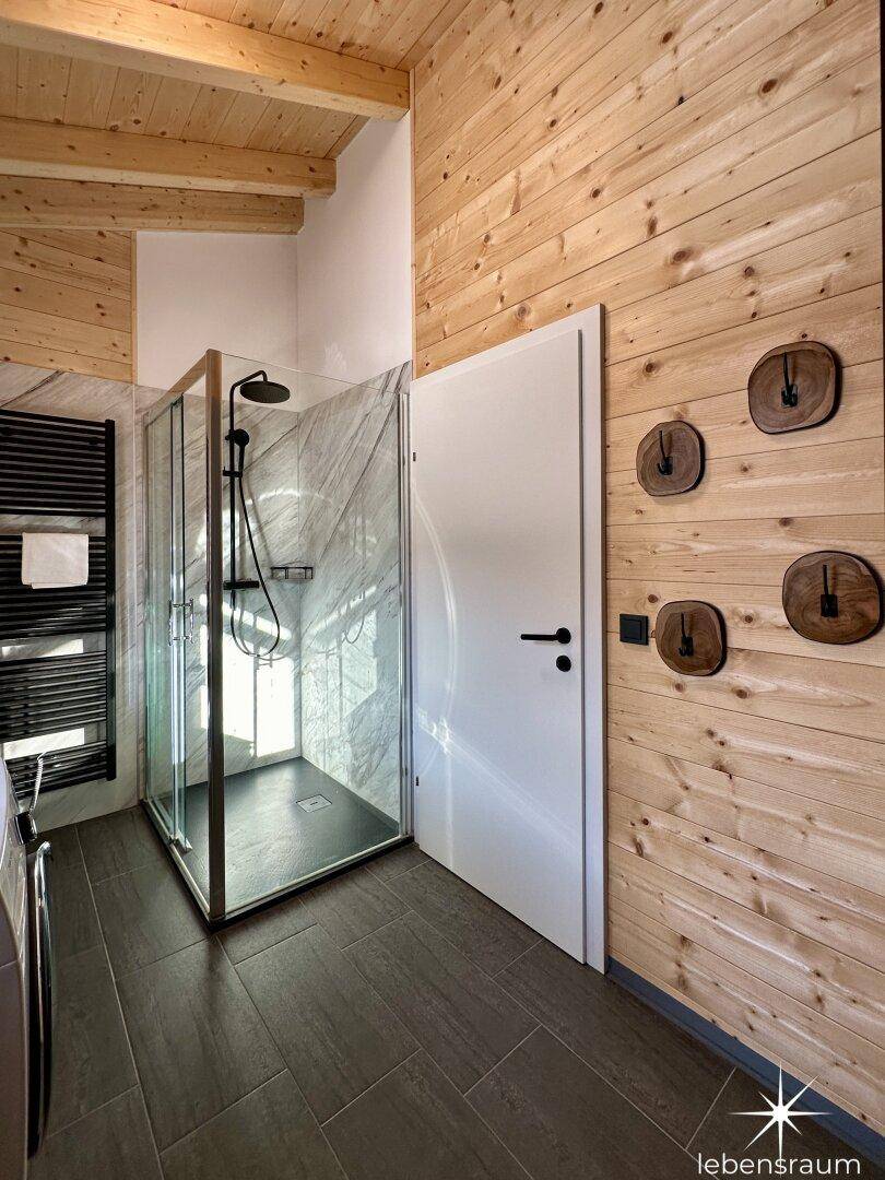 Badezimmer mit Duschkabine, beheiztem Handtuchhalter und Holzwänden.