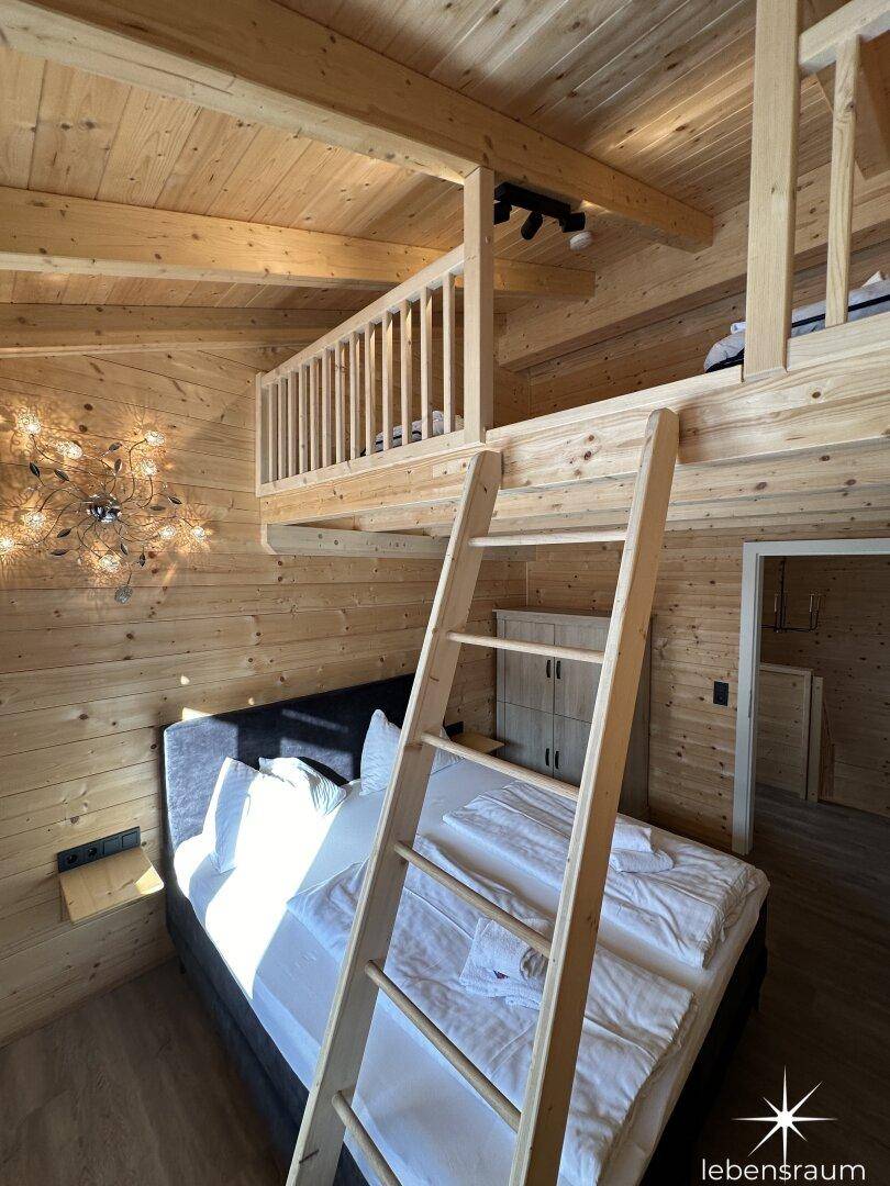 Gemütliches Schlafzimmer mit Holzwänden, Dachschräge und einer Leiter zum Hochbett.