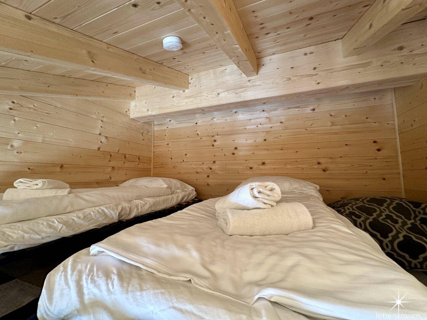 Zwei Einzelbetten in einem Schlafzimmer mit Holzwänden und sichtbaren Deckenbalken.