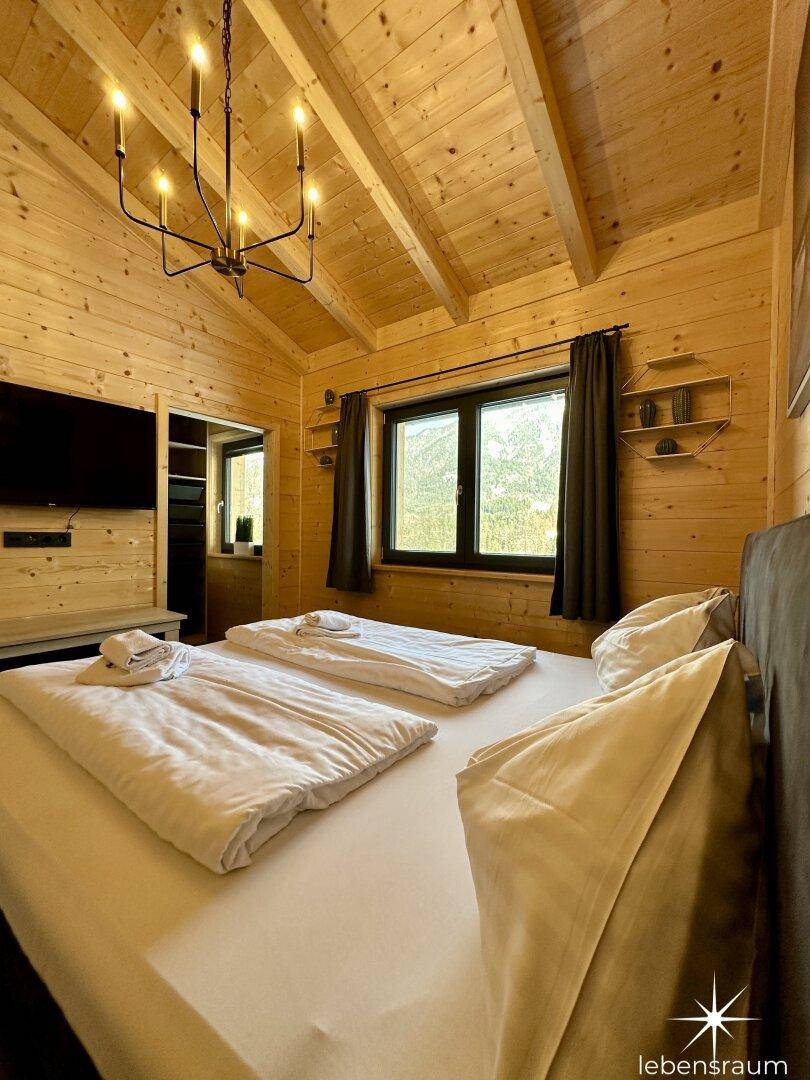 Gemütliches Schlafzimmer mit Holzwänden, Dachschräge und einem modernen Deckenleuchter.