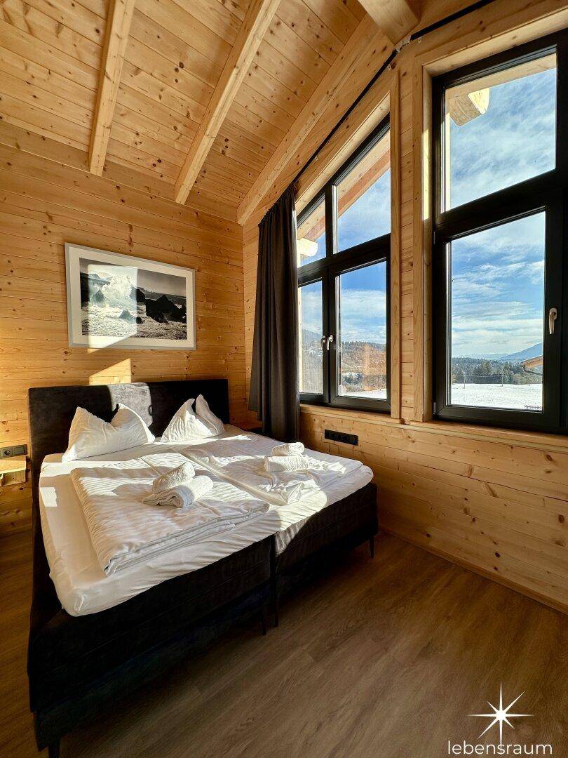 Helles Schlafzimmer mit Doppelbett, Holzwänden und großen Fenstern mit Bergblick.