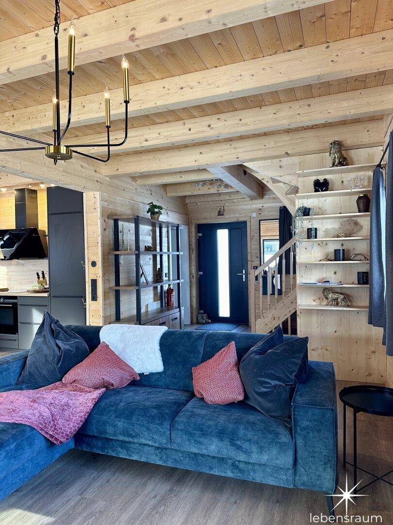Gemütliches Wohnzimmer mit blauem Sofa, Holzwänden und modernem Deckenleuchter.
