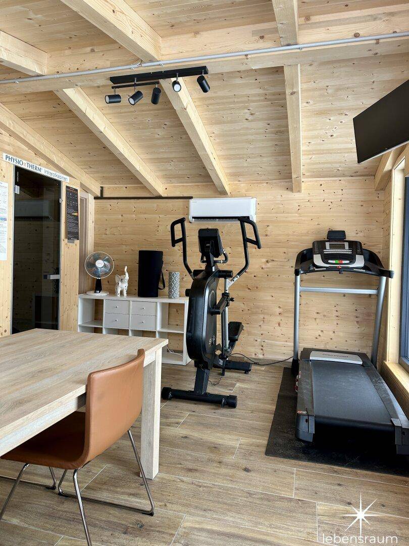 Fitnessbereich mit Laufband, Crosstrainer und einer Infrarotkabine für Wellness.