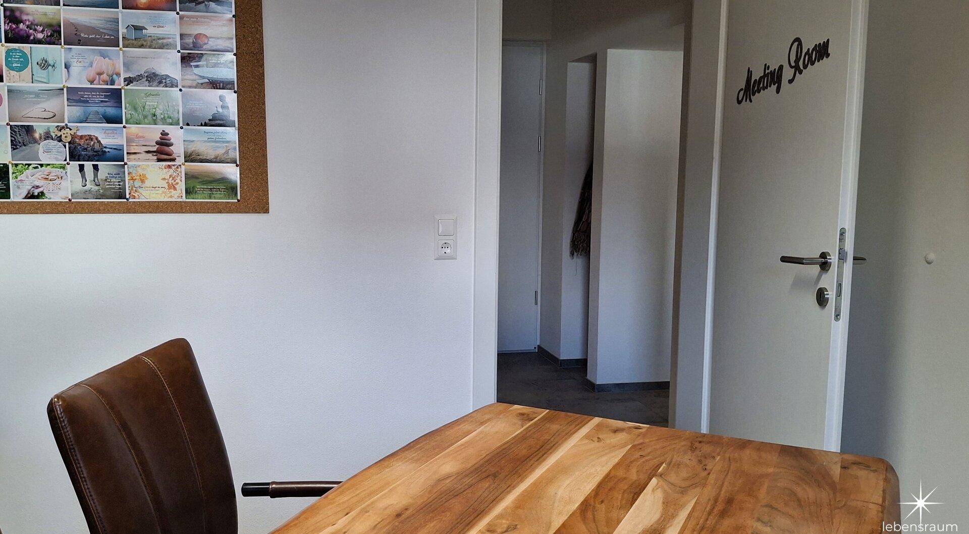 Bürobereich mit einem Holztisch und einer Tür, die zu einem weiteren Raum führt, ideal für Besprechungen.