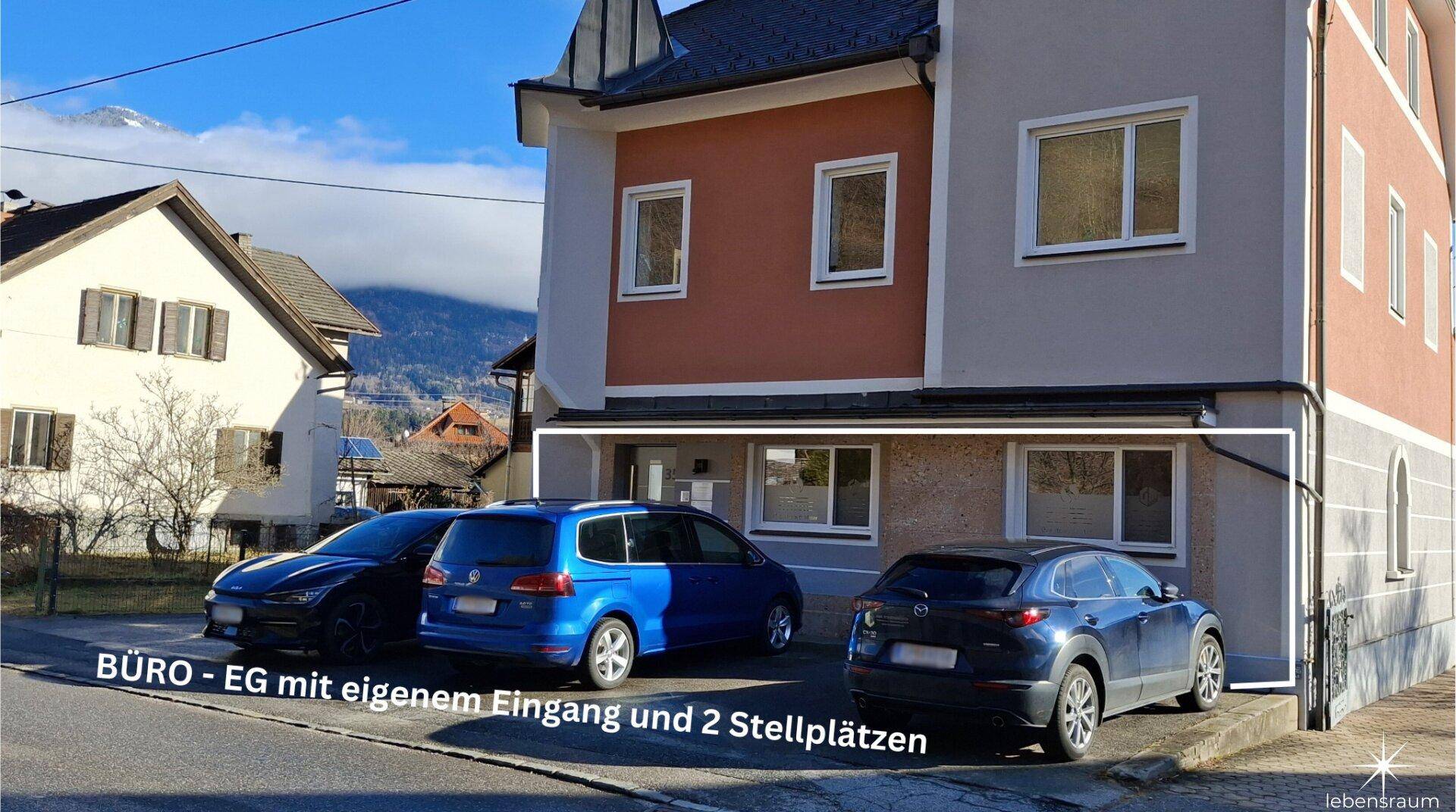 Außenansicht eines Gebäudes mit mehreren Parkplätzen davor und einem hervorgehobenen Eingangsbereich.