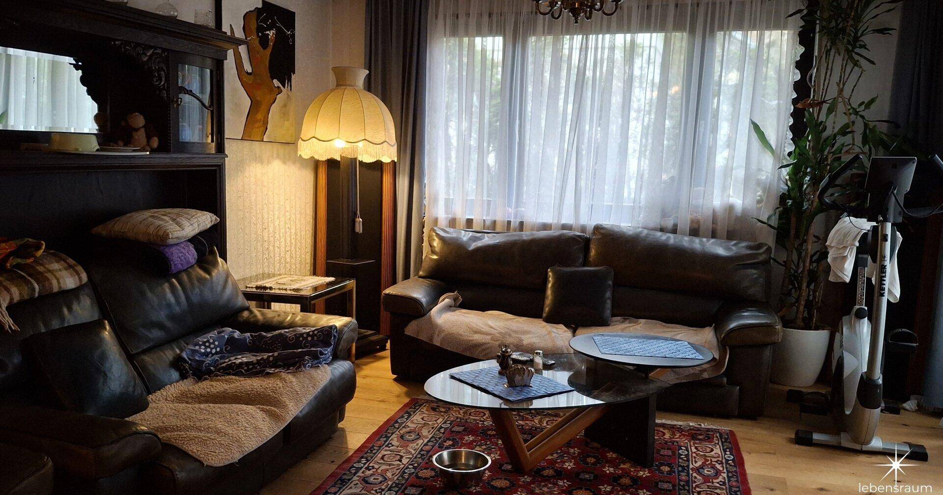 Wohnzimmer mit Ledersofas, Teppich und großem Fenster mit Vorhängen.