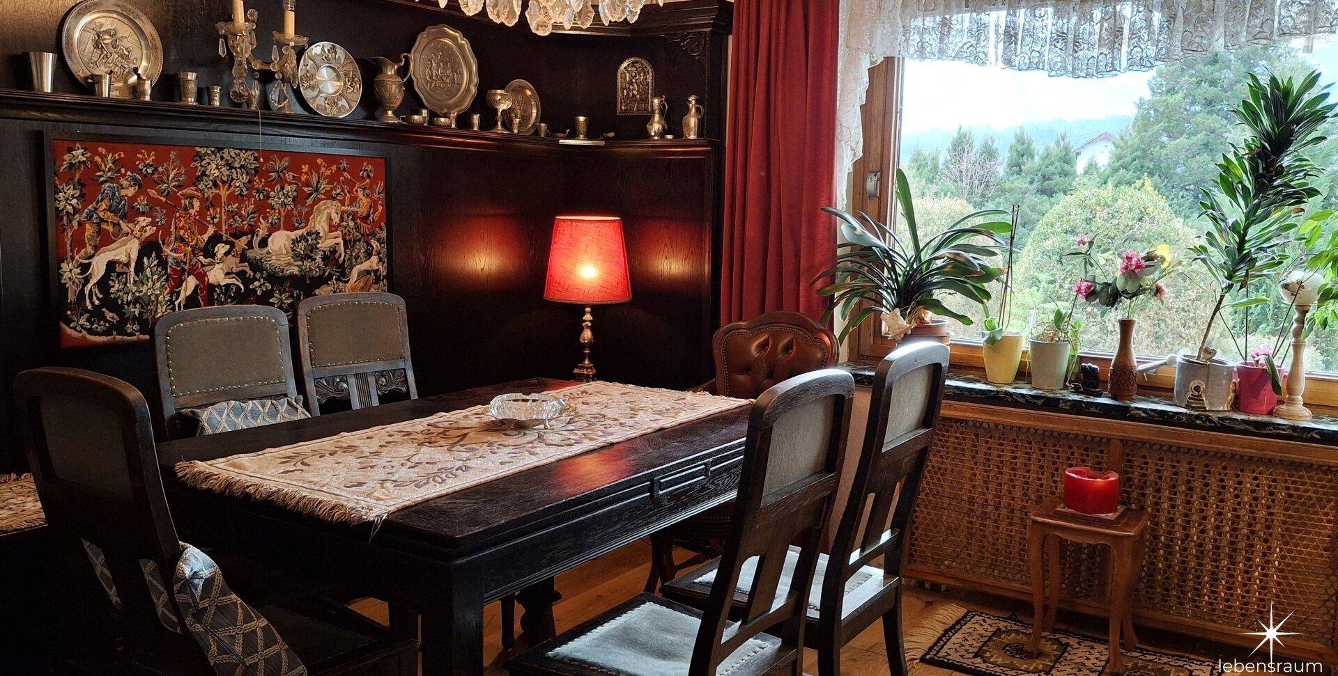 Eleganter Essbereich mit dunklem Holztisch, Wandteppich und Blick ins Grüne.