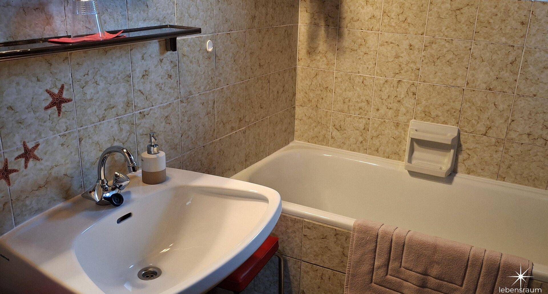 Badezimmer mit Badewanne, Waschbecken und gefliesten Wänden.