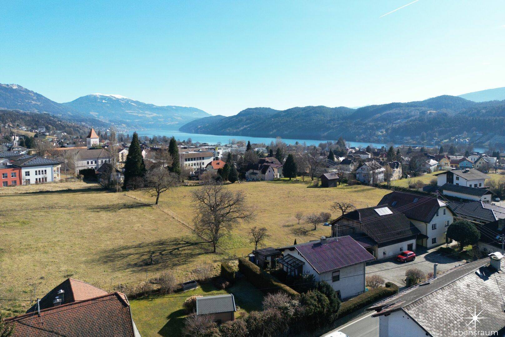 Weitläufiger Blick über die Landschaft mit See und Bergen unter blauem Himmel.