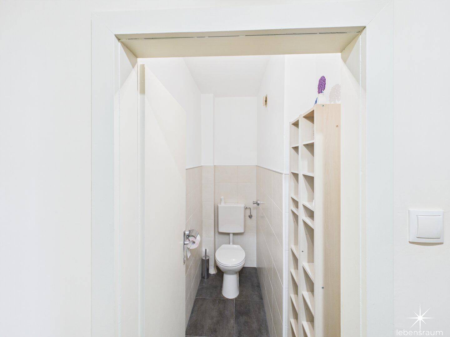 Separates WC mit Toilette, Fliesenboden und einem Regal für Utensilien.
