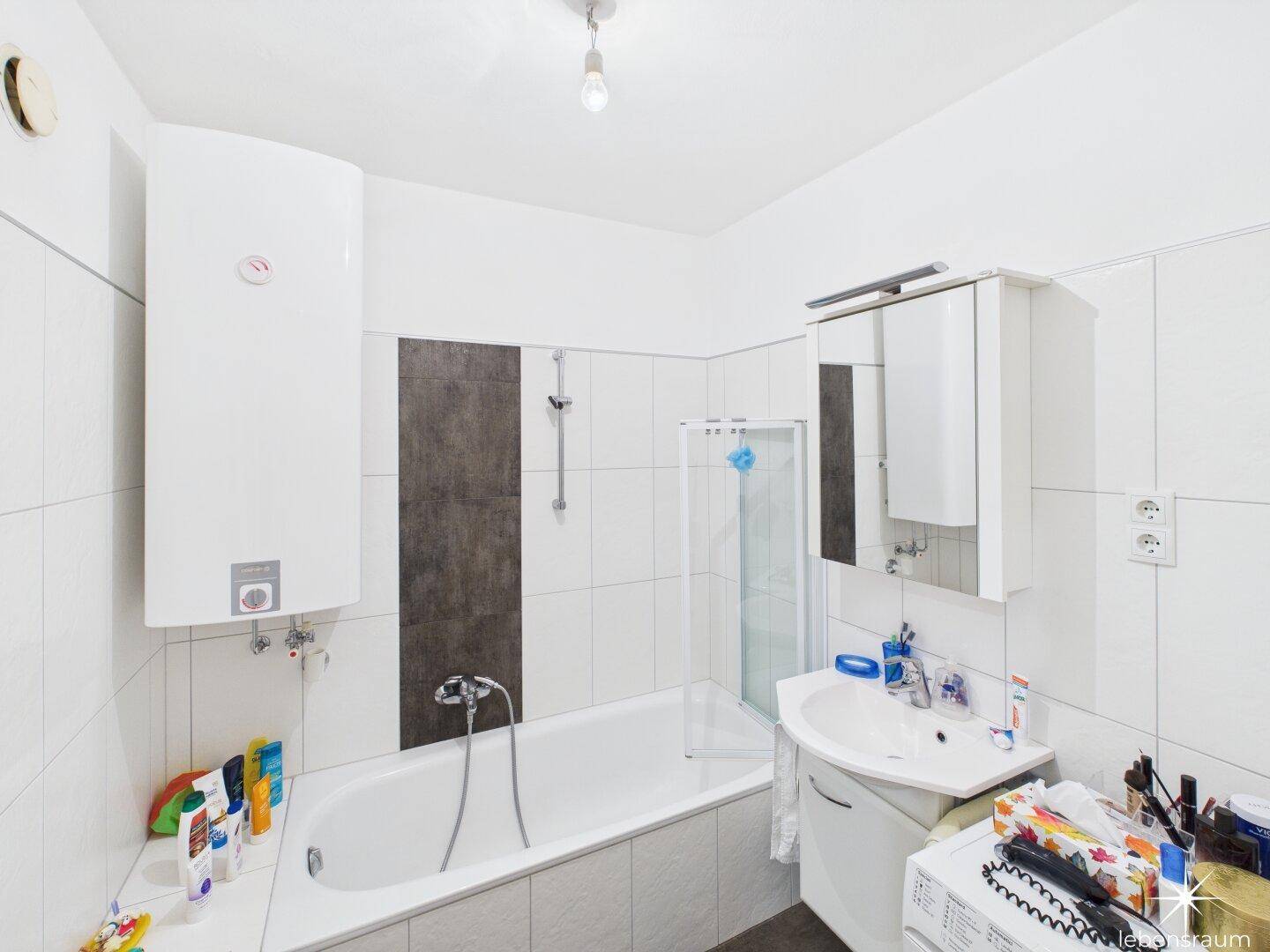 Badezimmer mit Badewanne, Waschbecken, Spiegelschrank und Warmwasserboiler.