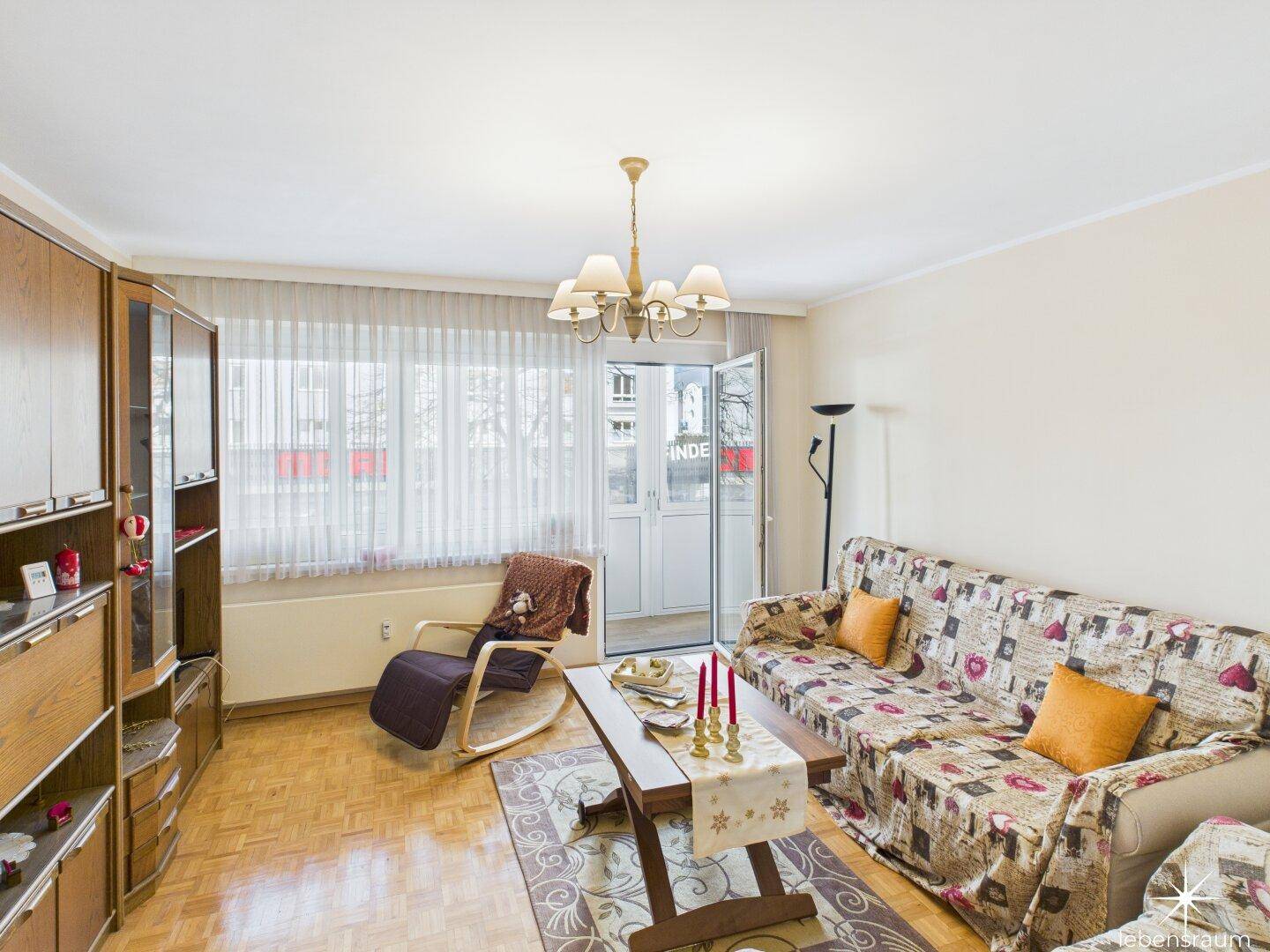 Wohnzimmer mit Sofa, Couchtisch und Zugang zu einem verglasten Balkon oder Wintergarten.