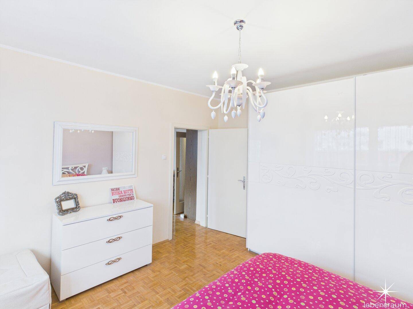 Schlafzimmer mit weißem Kleiderschrank, Kommode und hellem Parkettboden.