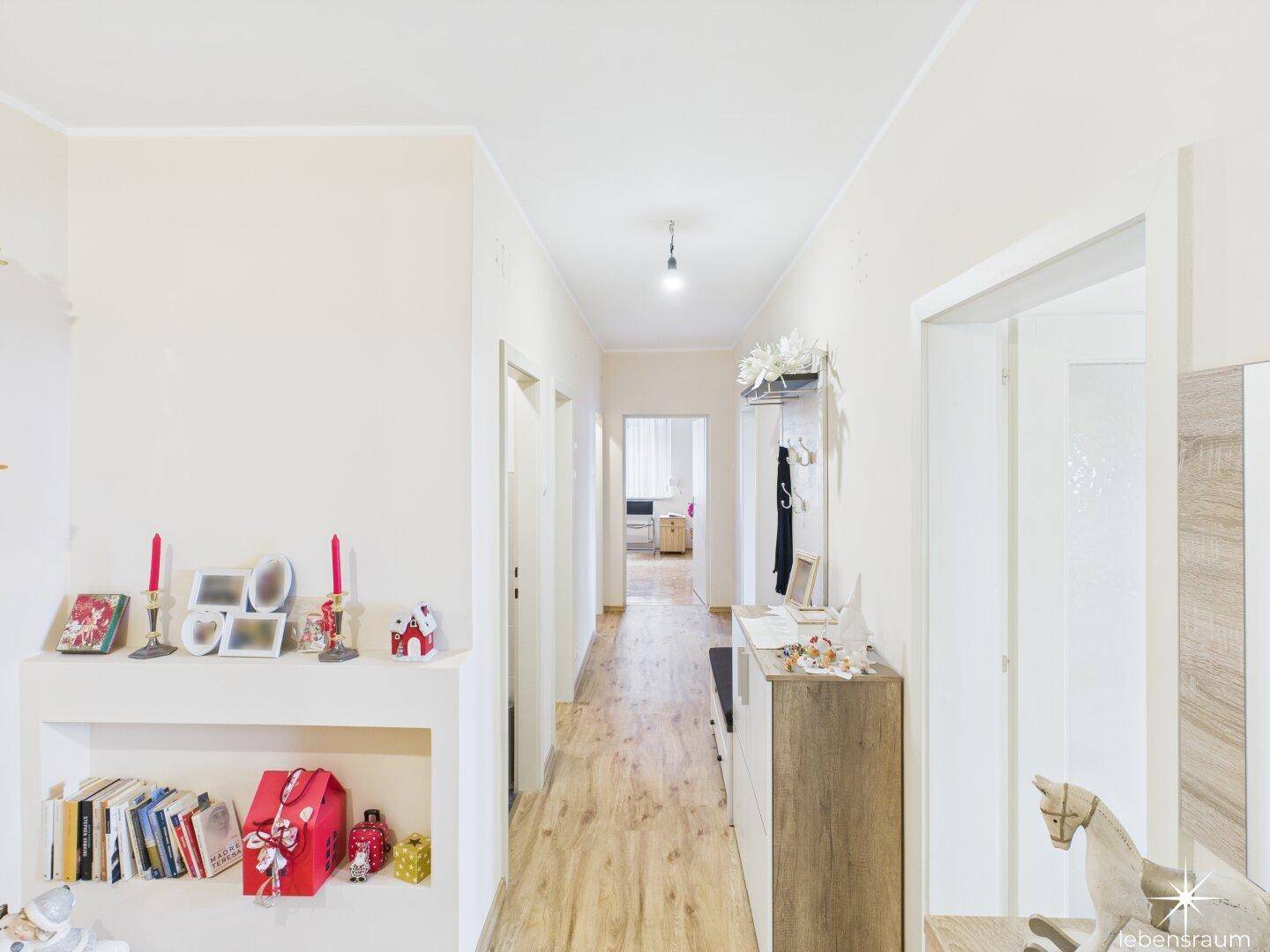 Langer Flur mit hellem Laminatboden, der zu verschiedenen Zimmern der Wohnung führt.