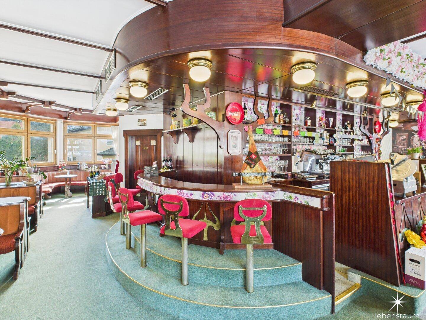 Detailansicht der Bar mit roten Barhockern, Holztheke und Regalen voller Flaschen und Gläser.