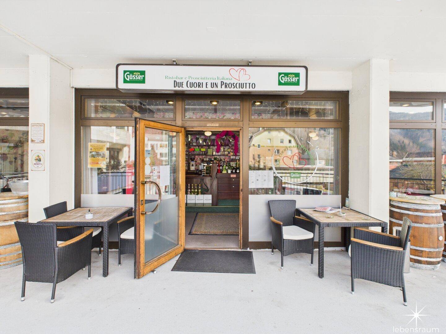 Eingangsbereich eines Restaurants mit Außenterrasse, Tischen und Stühlen.