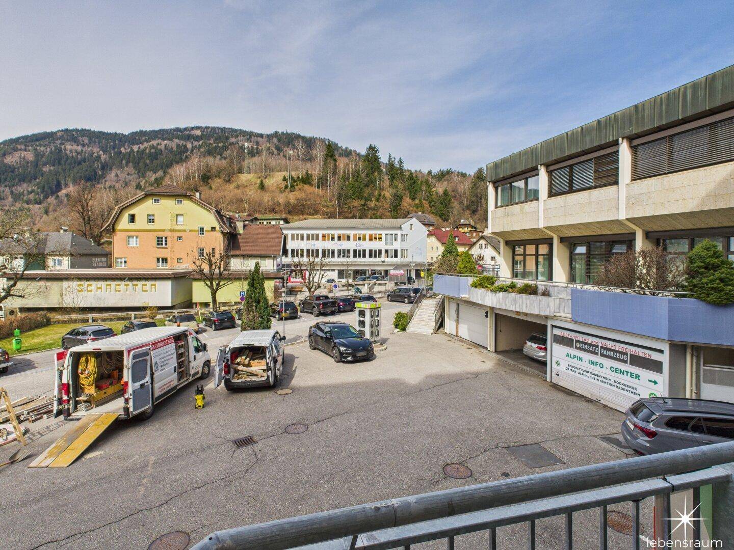 Außenansicht eines Gebäudekomplexes mit Parkplatz und umliegender Berglandschaft.