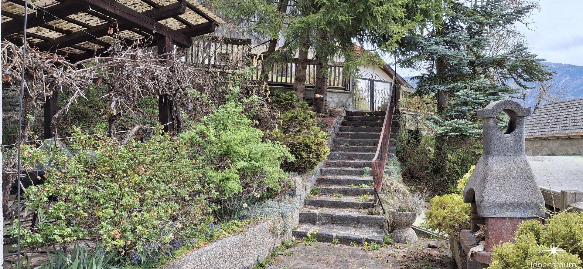 Steintreppe führt durch den Gartenbereich mit Bäumen und einem gemauerten Grill.
