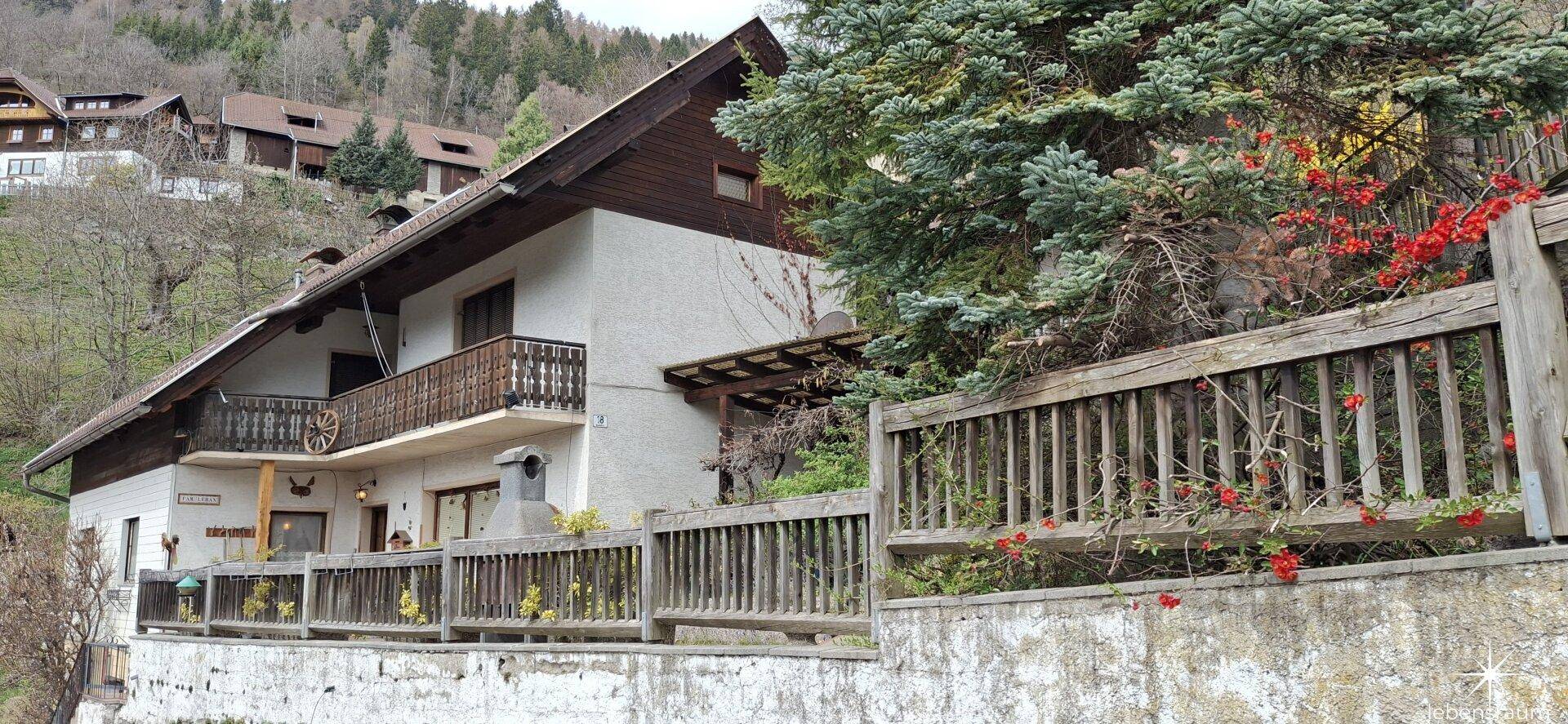 Traditionelles Haus mit Holzbalkonen und einer Fassade, umgeben von grüner Natur.