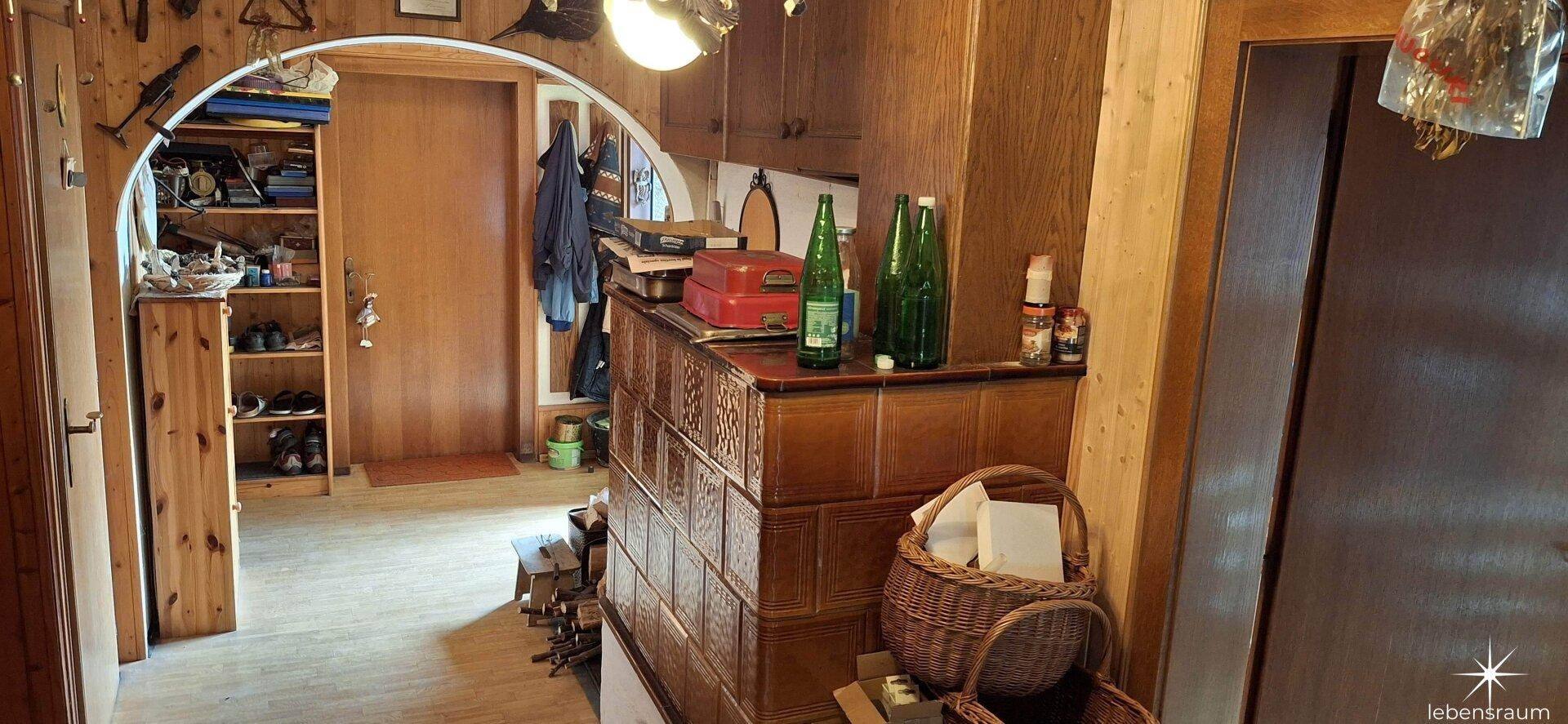 Eingangsbereich mit traditionellem Kachelofen und Holzelementen, führt zu weiteren Räumen.