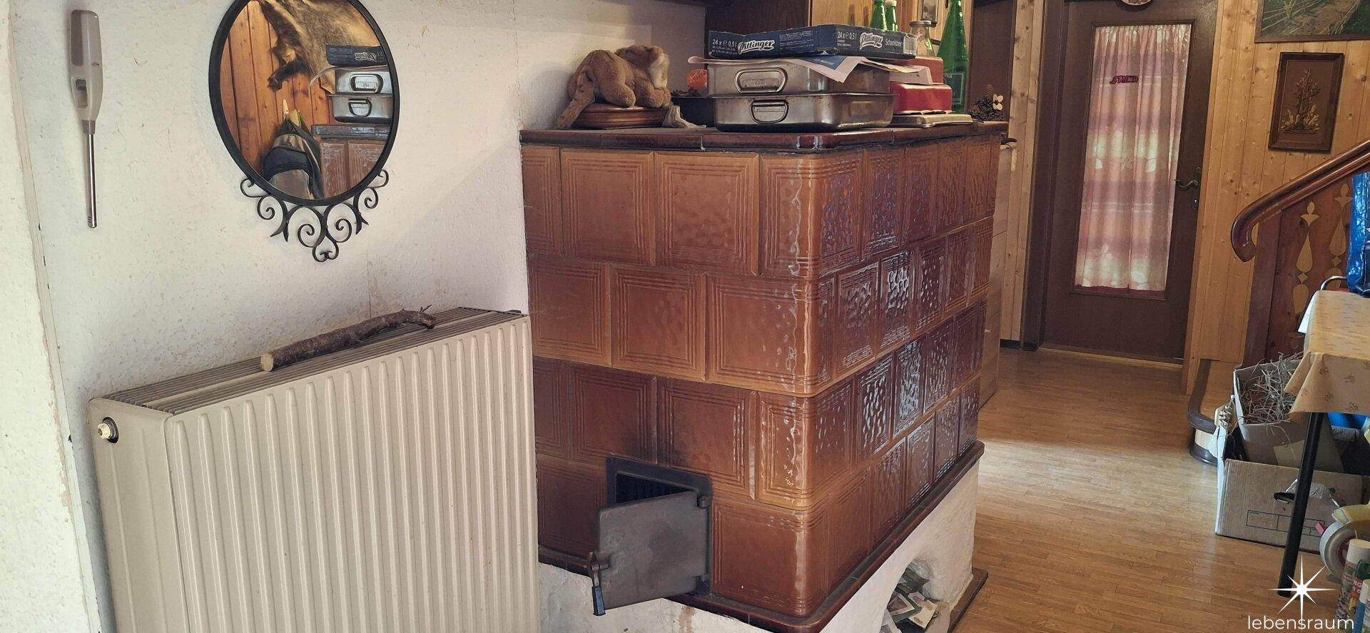 Traditioneller Kachelofen neben einem Heizkörper in einem rustikal eingerichteten Raum.