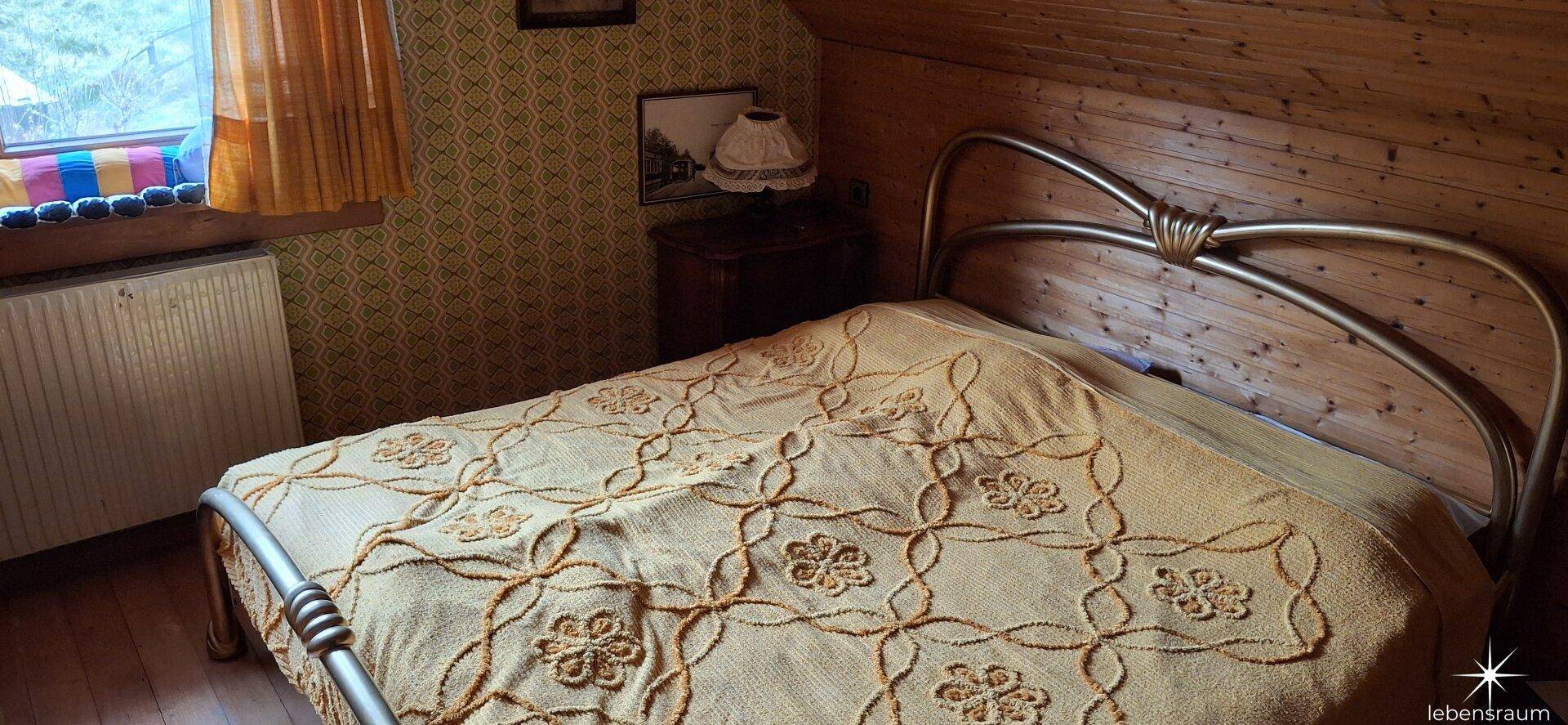 Schlafzimmer mit Metallbett und gemusterter Tapete, bietet einen Blick nach draußen.