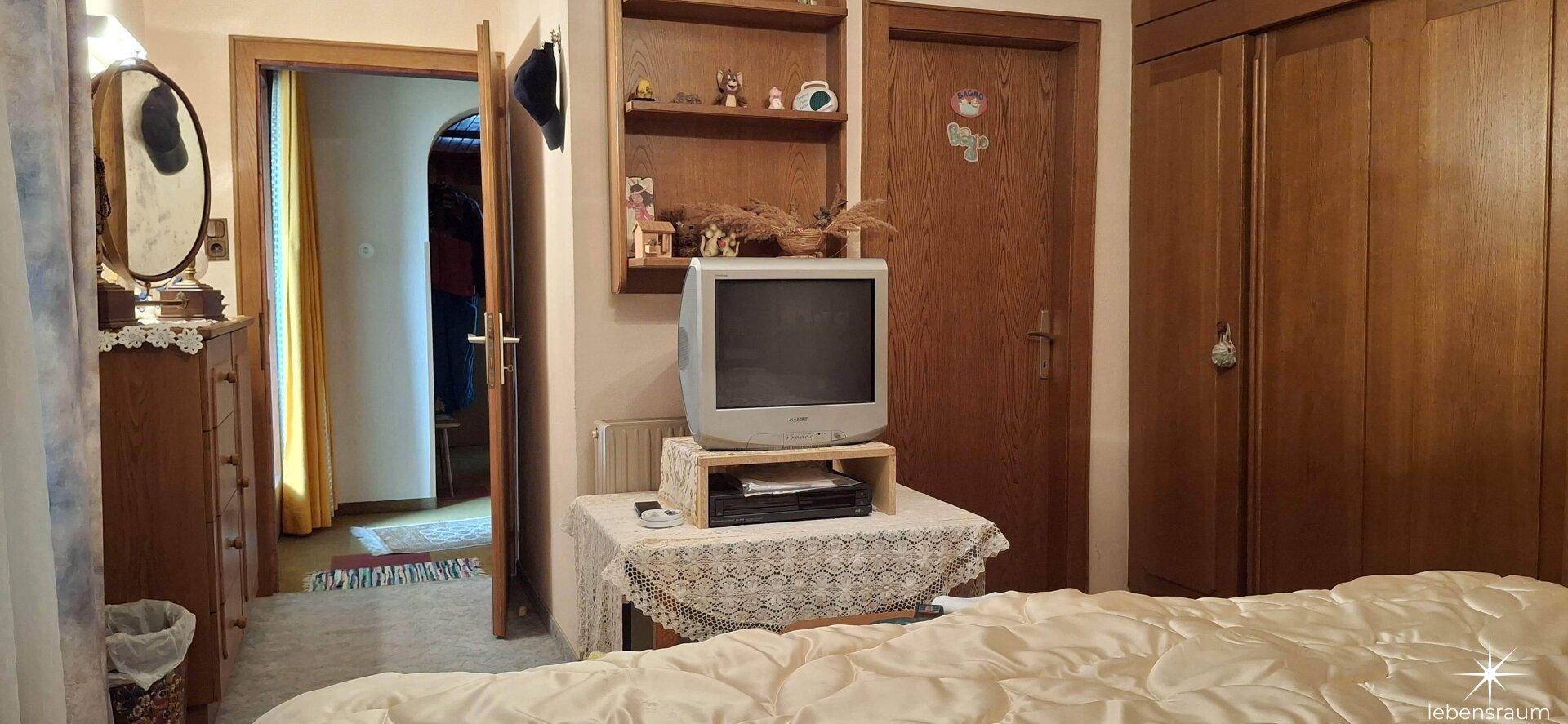 Schlafzimmer mit traditionellem Bett, Fernseher und Holzmöbeln, gemütlich eingerichtet.
