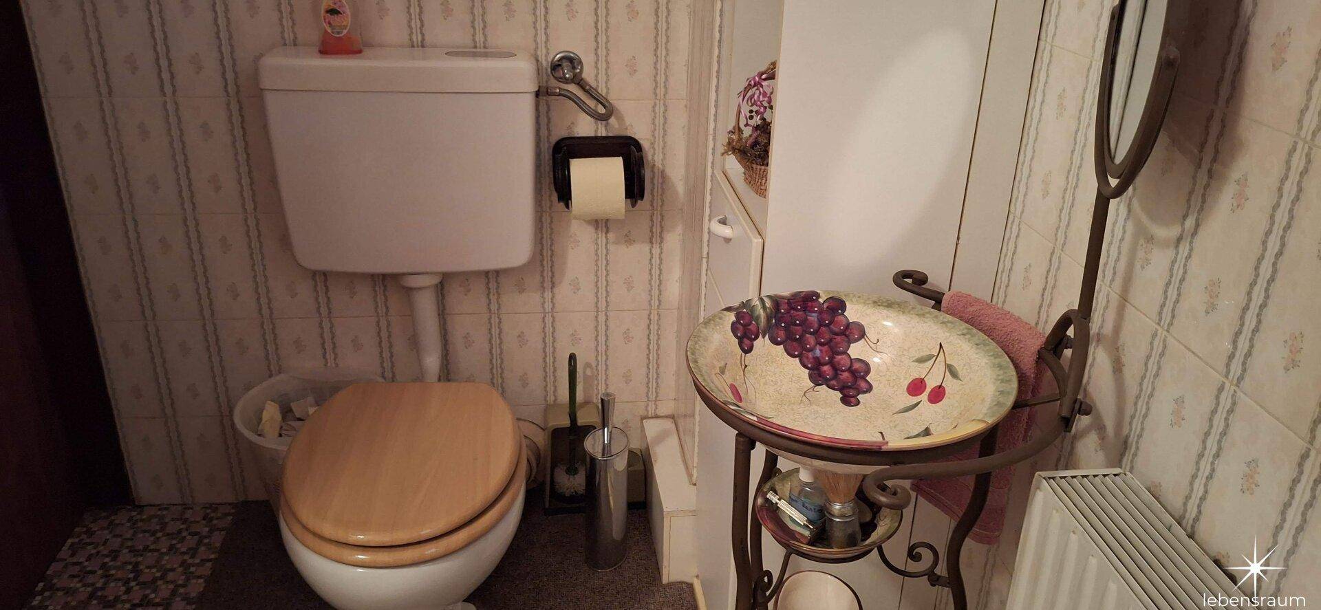 Kleines WC mit Toilette und einem handbemalten Waschbecken, gefliesten Wänden.