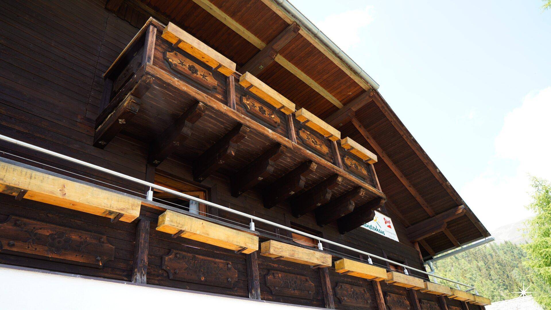 Traditioneller Holzbalkon mit geschnitzten Details an einer alpinen Gebäudefassade.