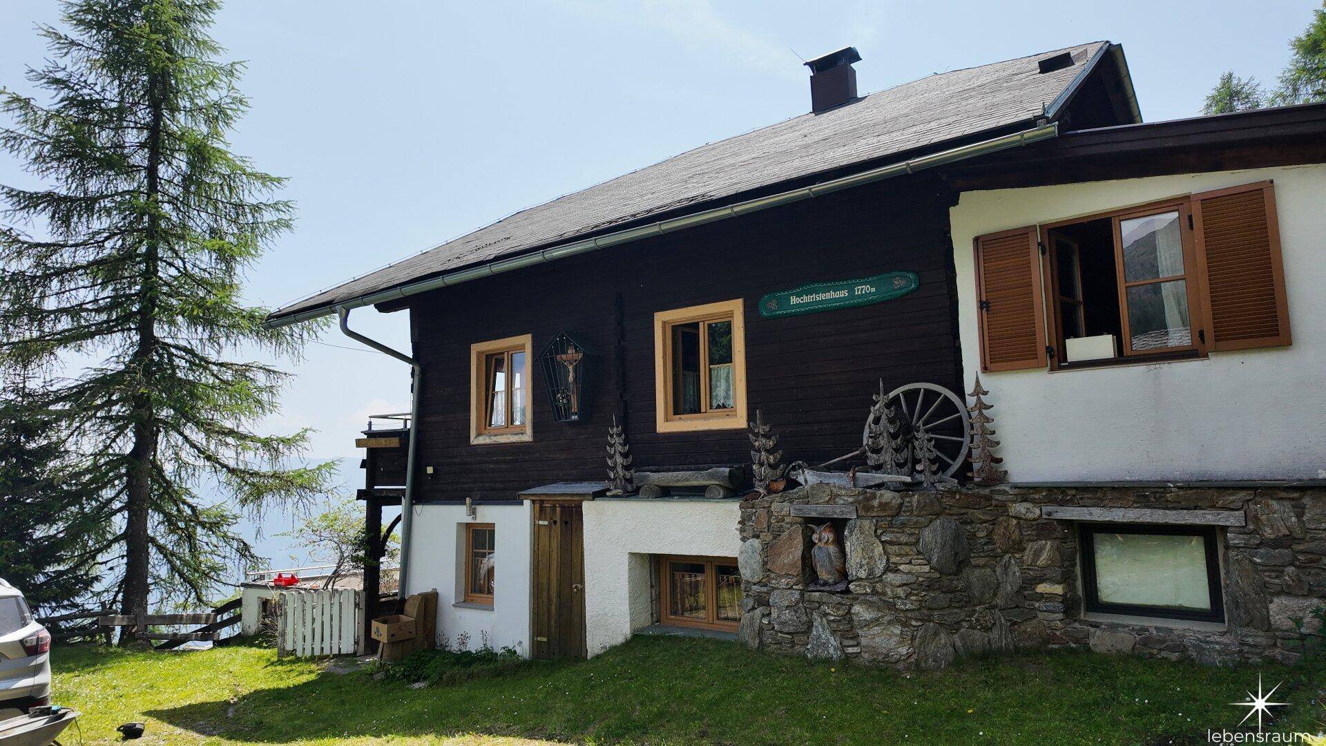 Traditionelles Holzhaus mit Steinfundament und grüner Umgebung in den Bergen.