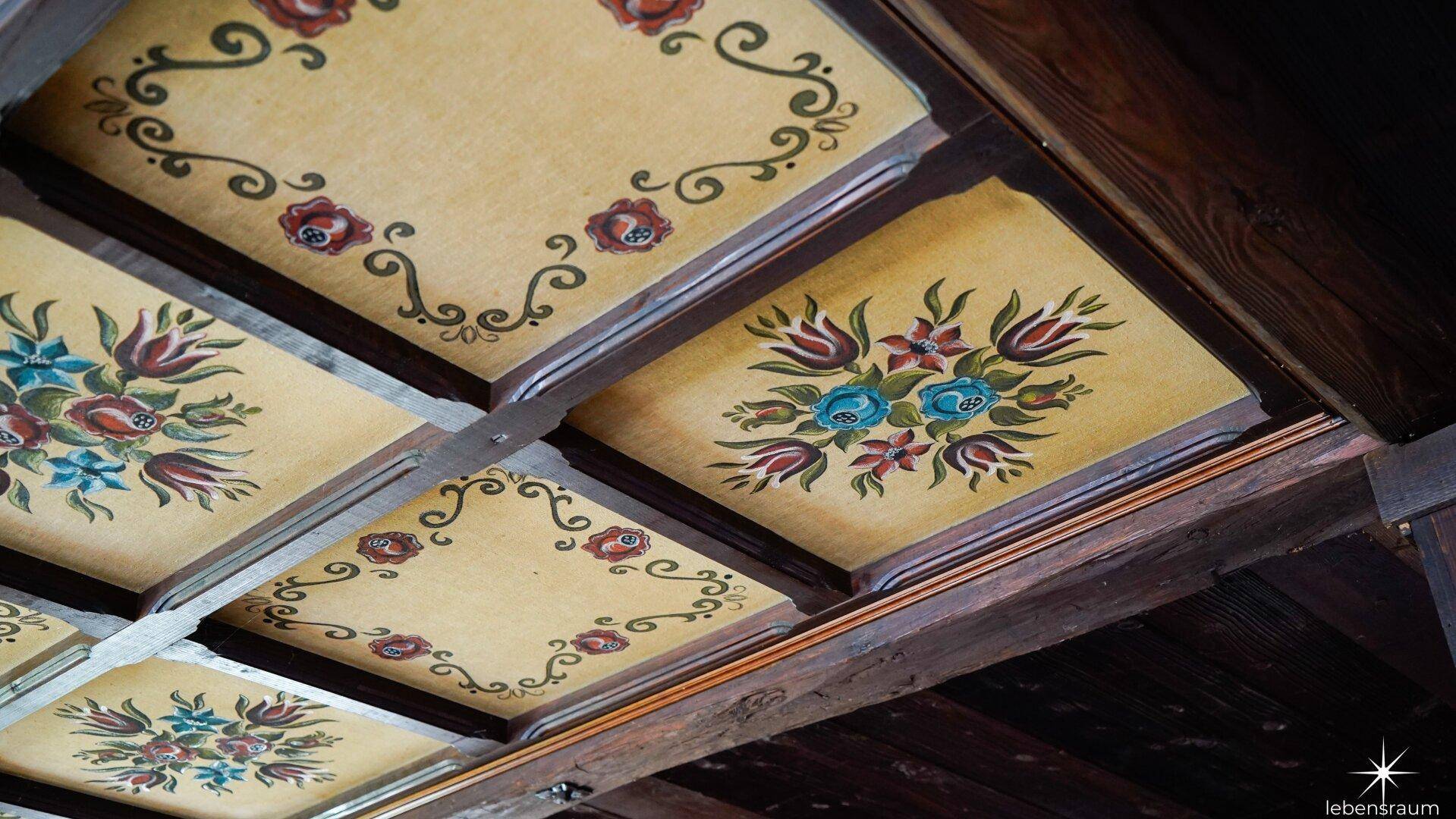 Holzbalkendecke mit handgemalten floralen Mustern in traditionellem Stil.