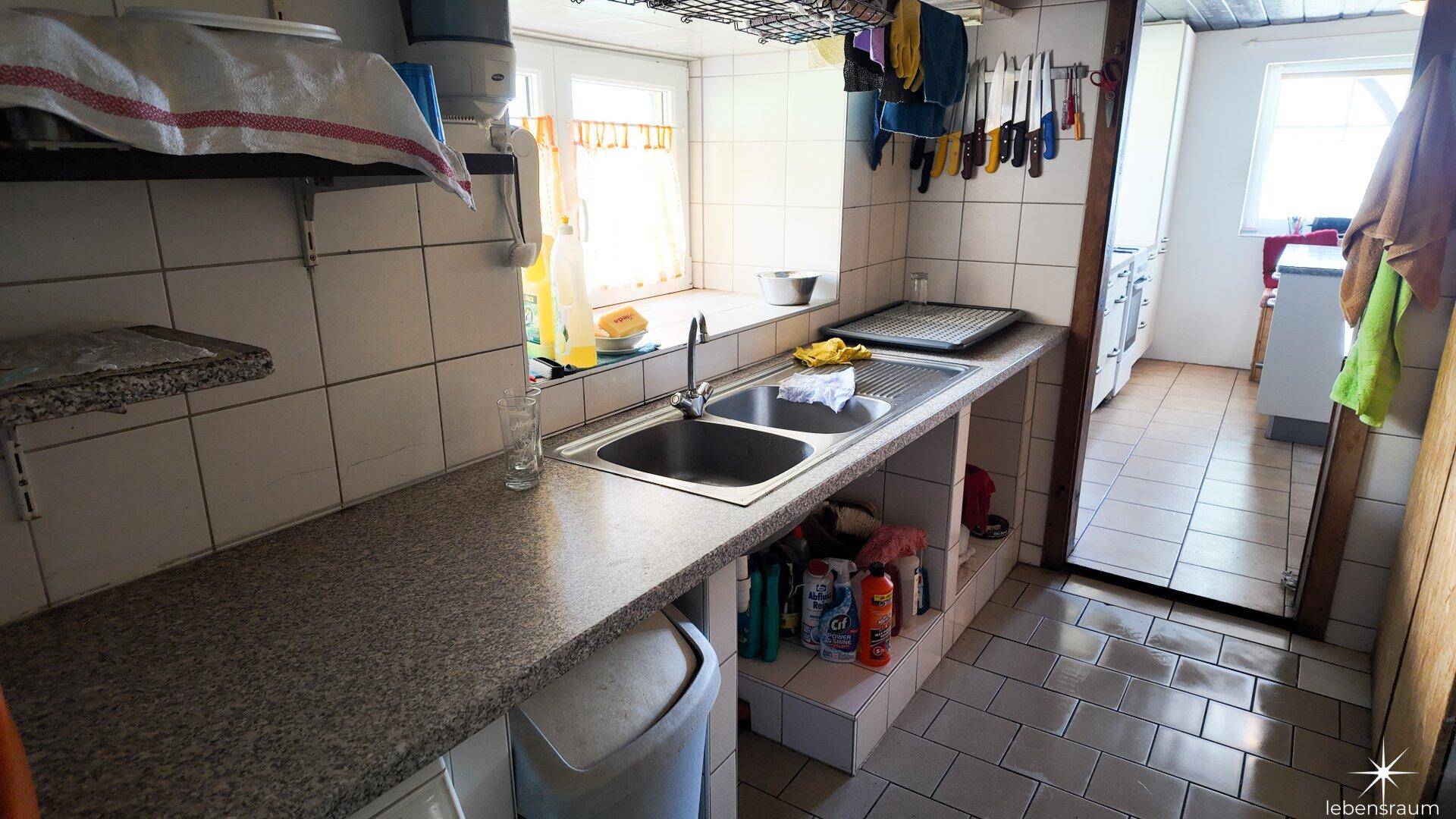 Einfache Küche mit Doppelspüle, gefliestem Spritzschutz und funktionaler Arbeitsplatte.
