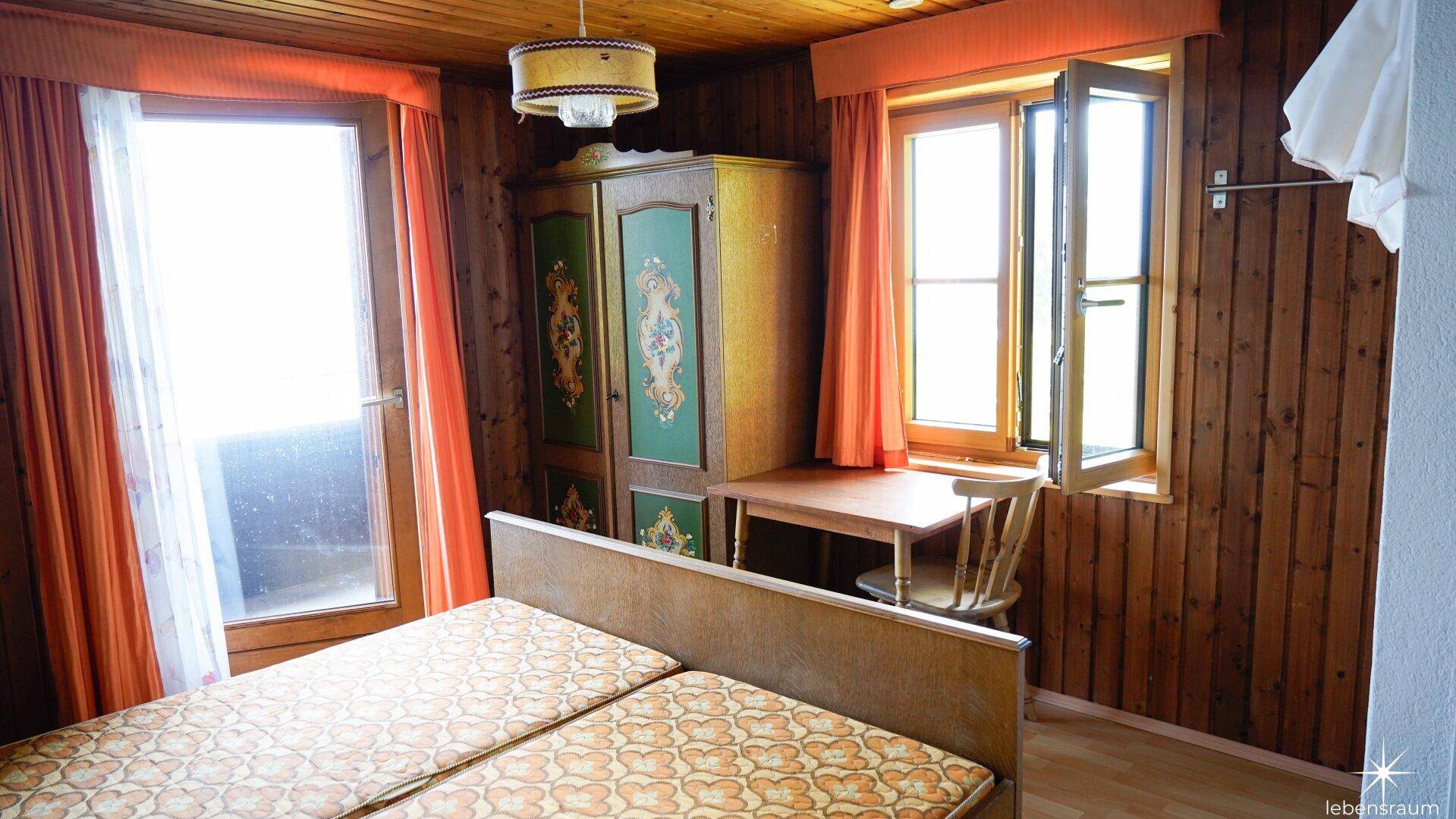 Schlafzimmer mit Holztäfelung, Doppelbett und einem bemalten Kleiderschrank.