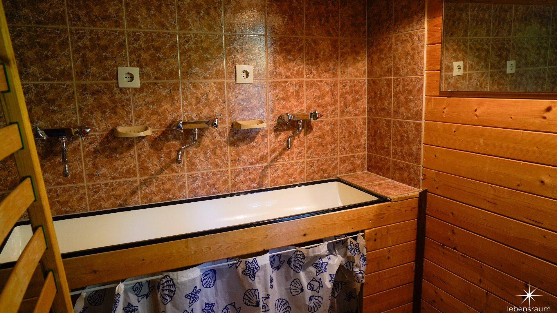 Badezimmer mit langer Badewanne, braunen Fliesen und Holztäfelung.