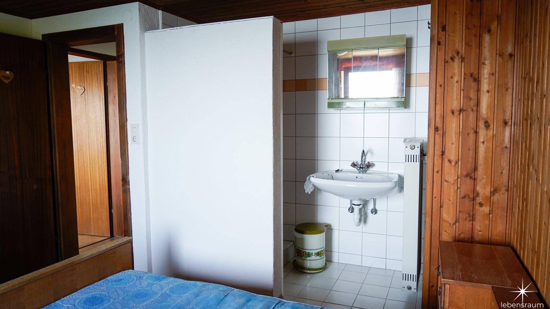 Kleiner Badezimmerbereich mit Waschbecken, Spiegelschrank und Fliesenboden neben dem Schlafzimmer.