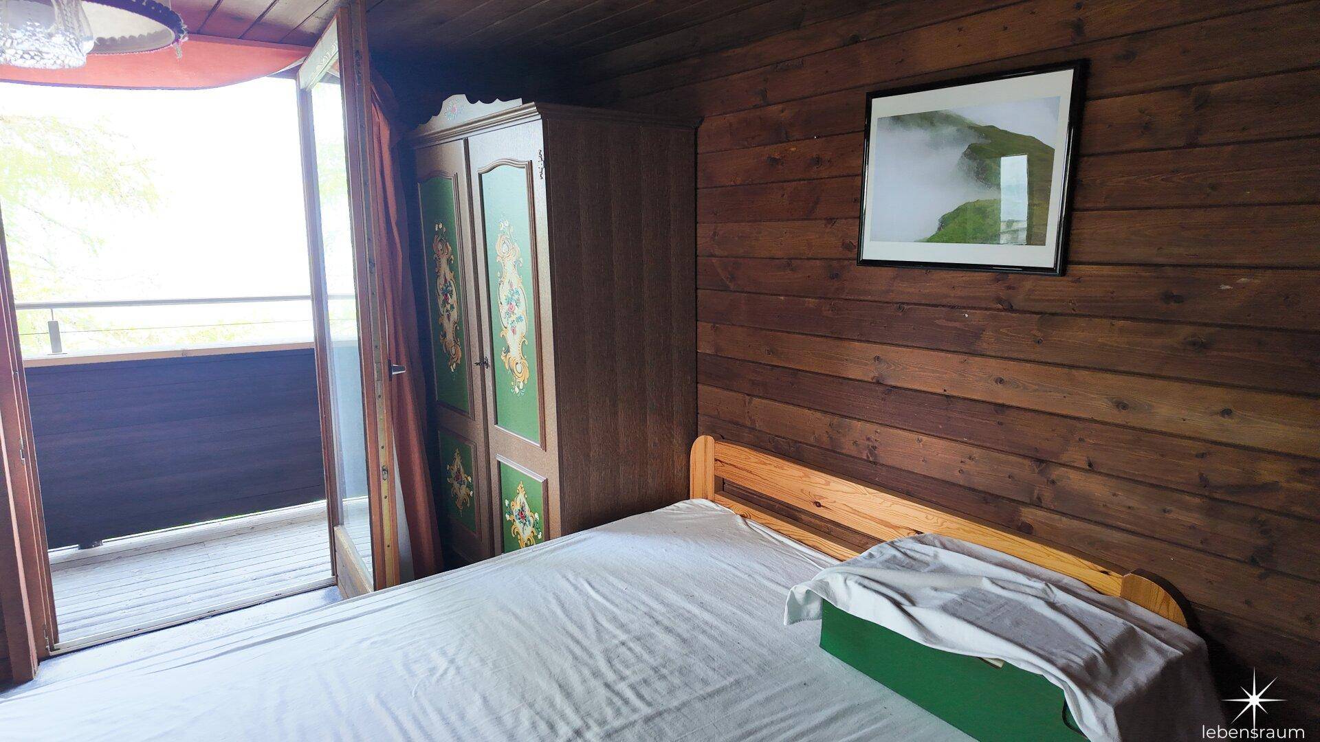 Gemütliches Schlafzimmer mit Holzwänden, Bett und Zugang zum Außenbereich.