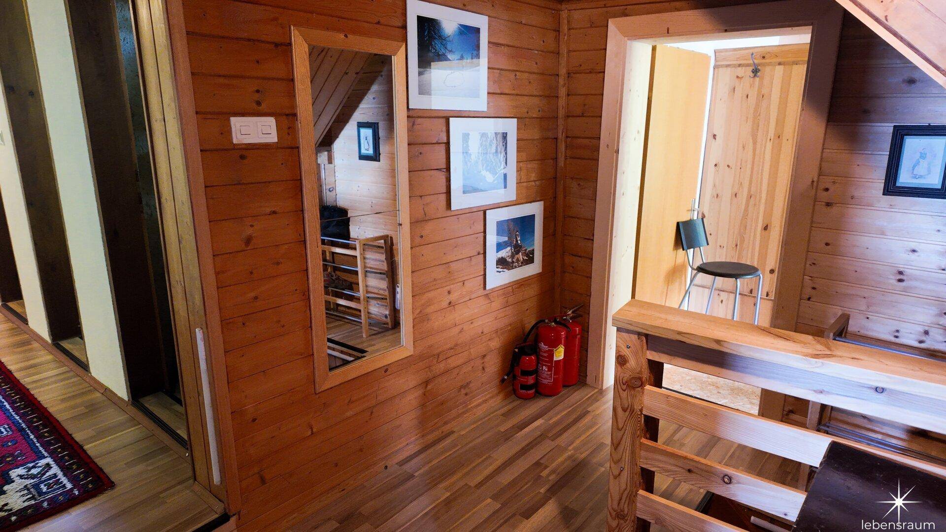 Flur mit Holzboden und -wänden, einem großen Spiegel und gerahmten Bildern.