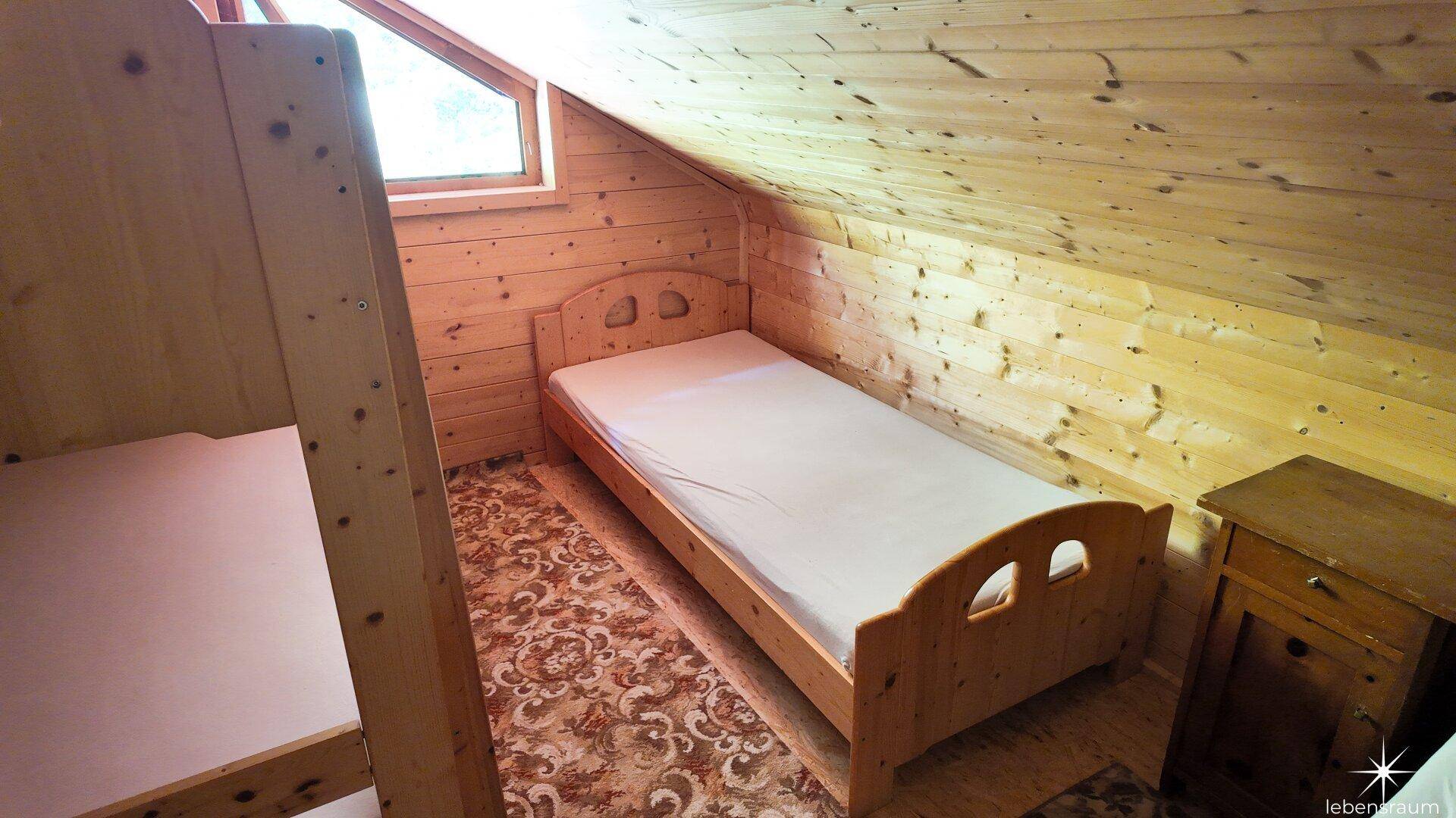 Gemütliches Schlafzimmer im Dachgeschoss mit Holzvertäfelung, Etagenbetten und einem Einzelbett.