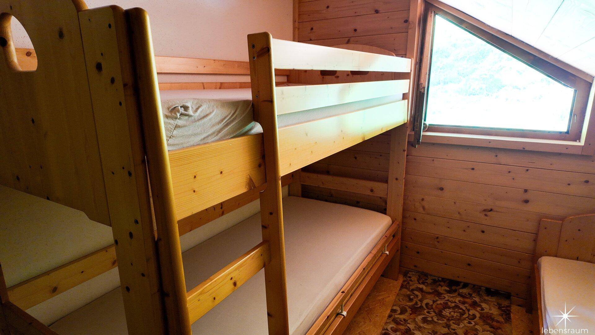 Detailansicht der Etagenbetten in einem rustikalen Schlafzimmer mit Holzvertäfelung und Dachfenster.