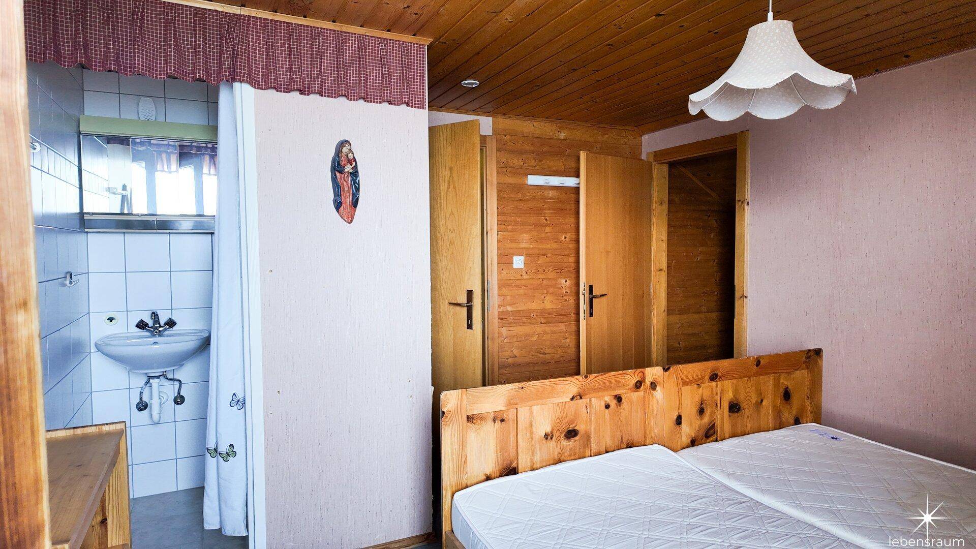 Schlafzimmer mit Doppelbett und integriertem, einfachem Waschbereich mit Waschbecken und Spiegel.
