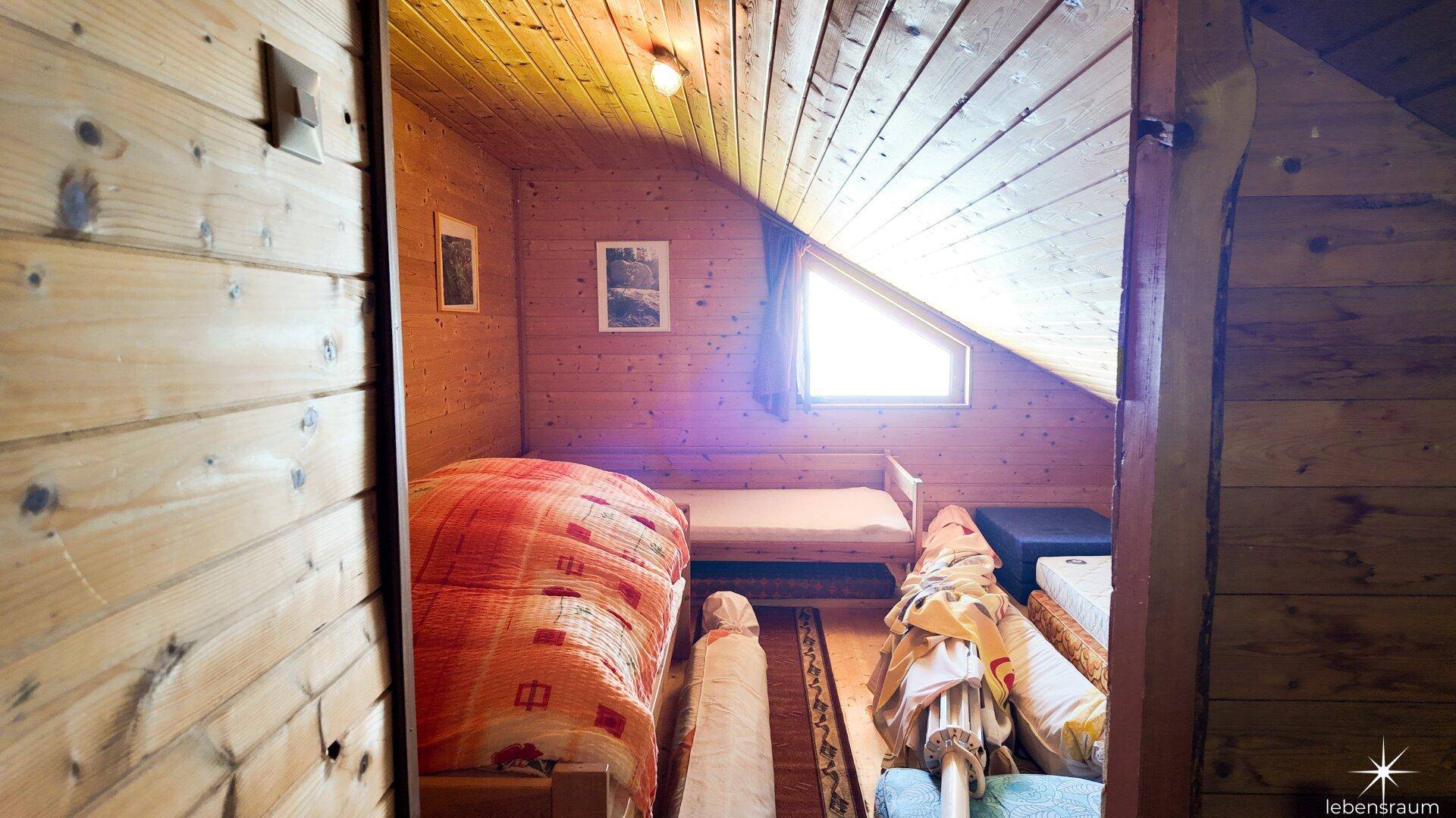 Rustikales Schlafzimmer im Dachgeschoss mit Einzelbett, Holzvertäfelung und schräger Decke.