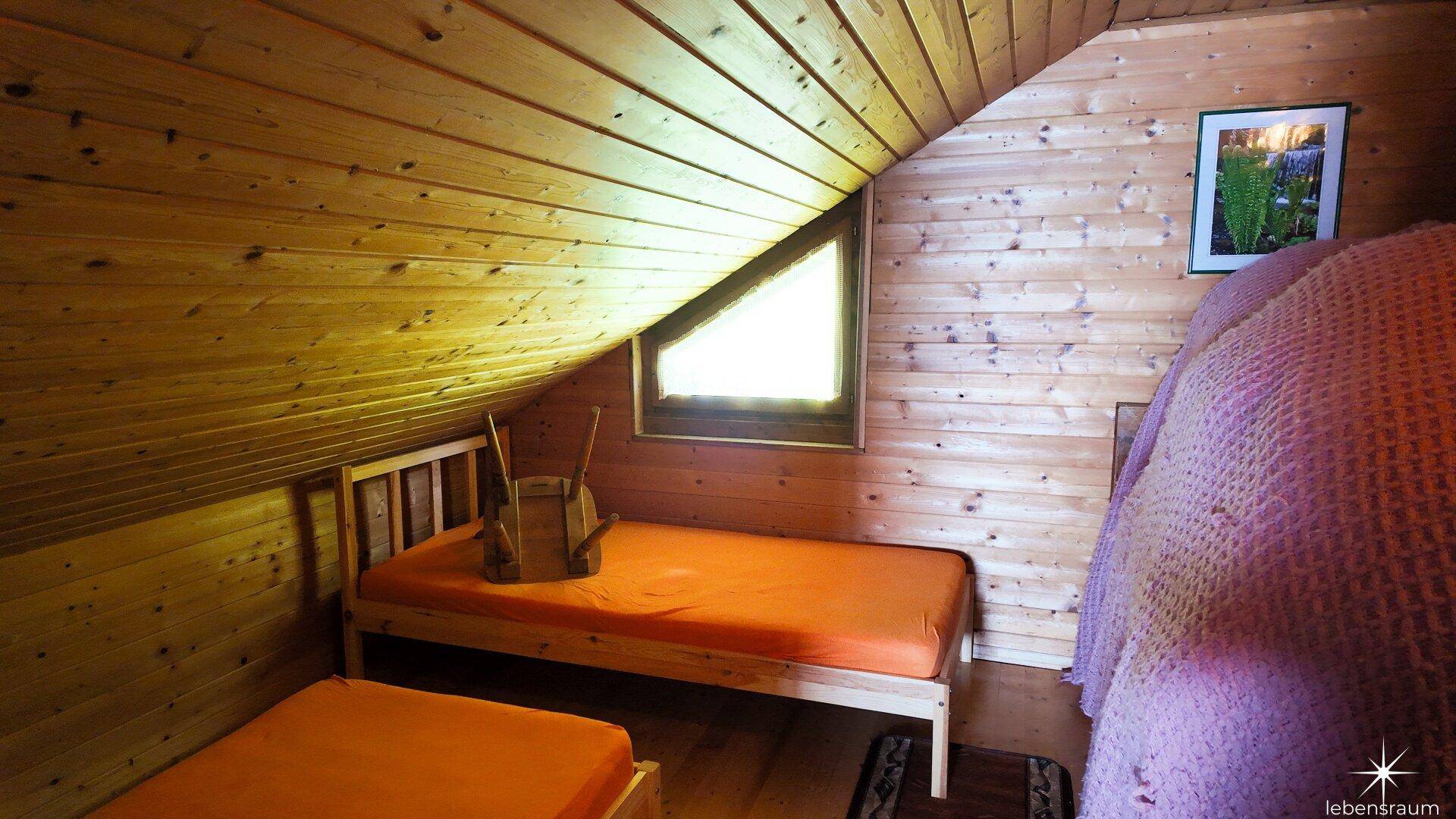 Helles Schlafzimmer im Dachgeschoss mit zwei Einzelbetten, Holzvertäfelung und Dachschräge.
