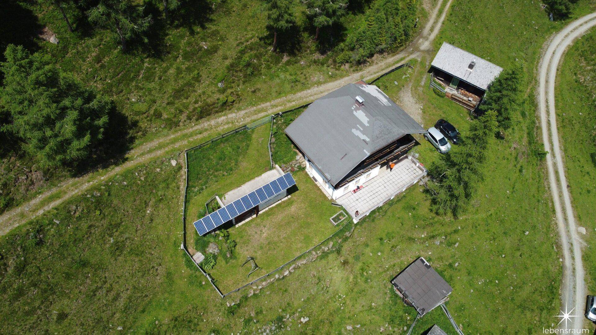 Luftaufnahme eines Anwesens in grüner Berglandschaft mit Photovoltaikanlage auf dem Grundstück.