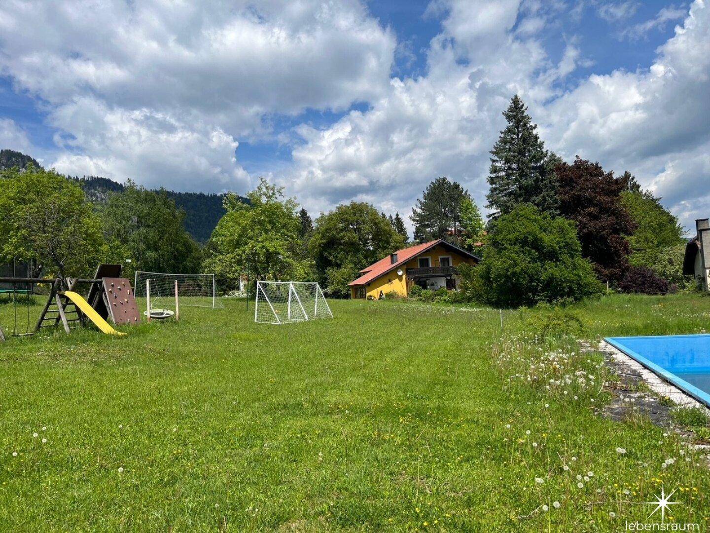Weitläufiger Gartenbereich mit Spielgeräten, Pool und malerischem Bergblick.
