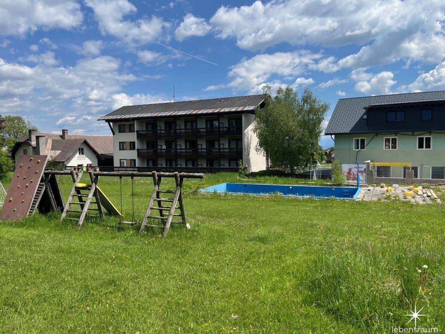 Großer Garten mit Spielplatz, Pool und Mehrfamilienhäusern im Hintergrund.