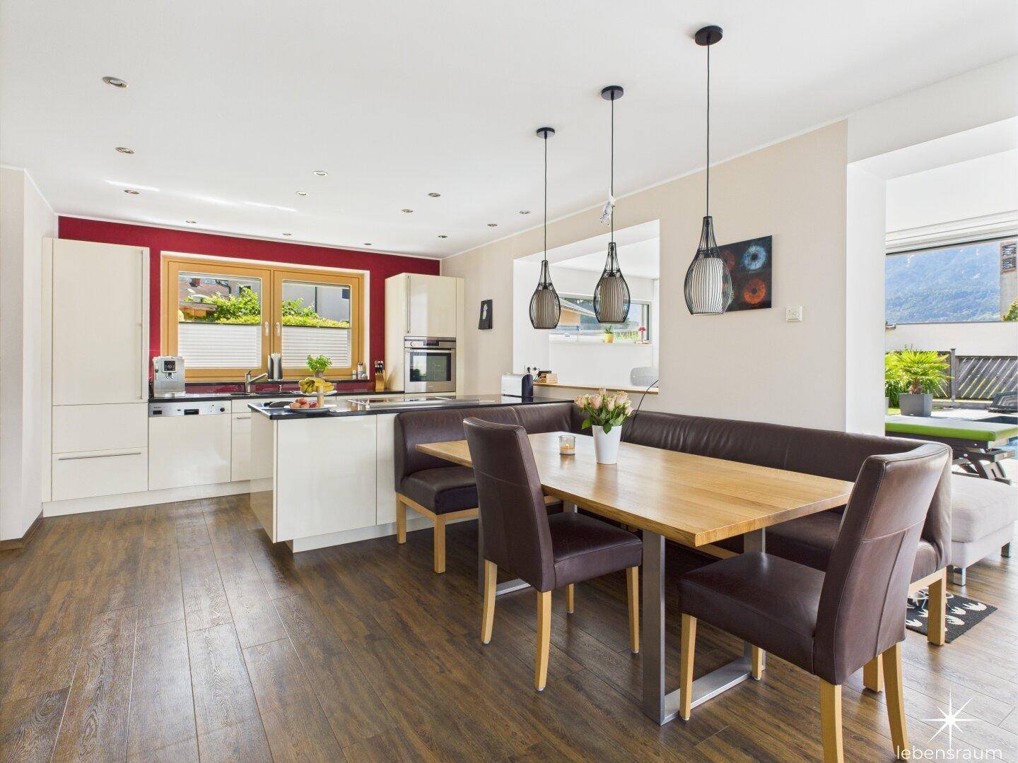 Moderne Wohnküche mit Essbereich, Holzboden und roten Akzentwänden.