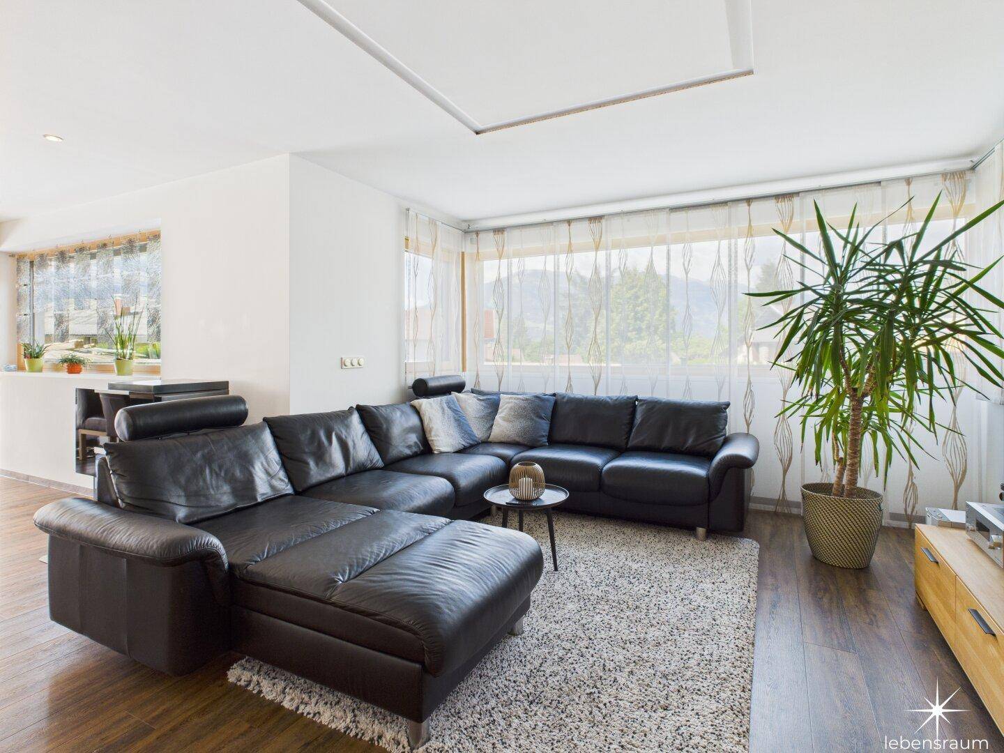 Helles Wohnzimmer mit Ecksofa, Teppich und Blick ins Grüne.