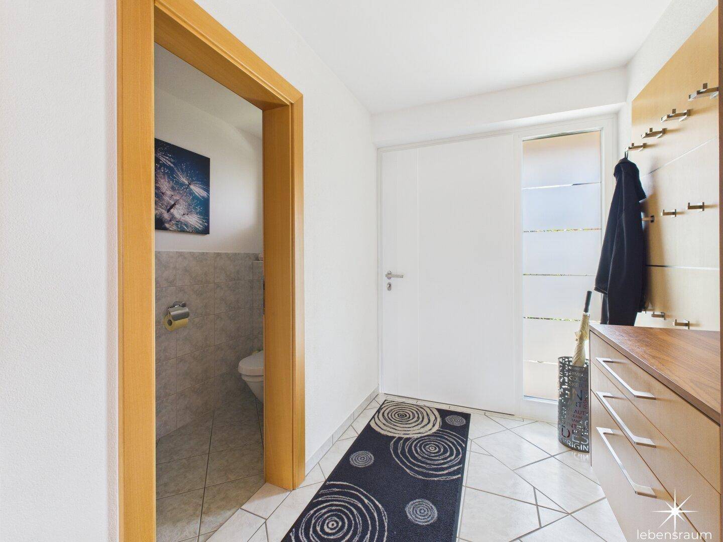 Eingangsbereich mit Fliesenboden, Garderobe und Zugang zu einem Gäste-WC.