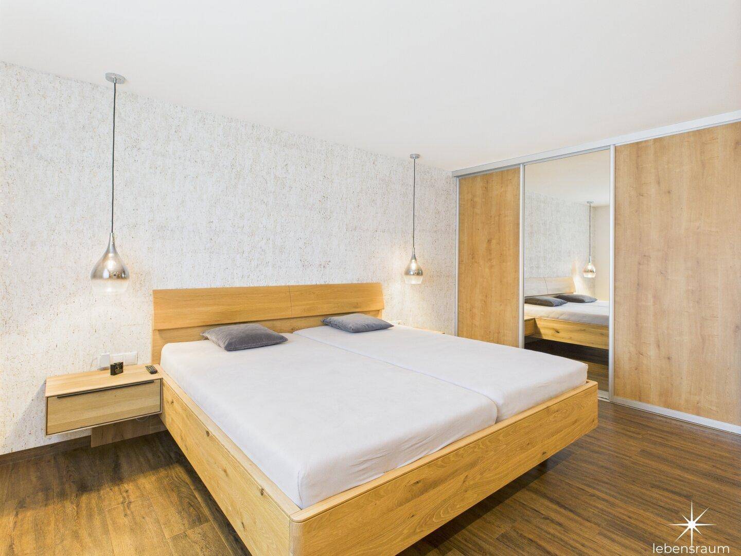 Modernes Schlafzimmer mit Holzbett, Schiebetürenschrank und Holzboden.