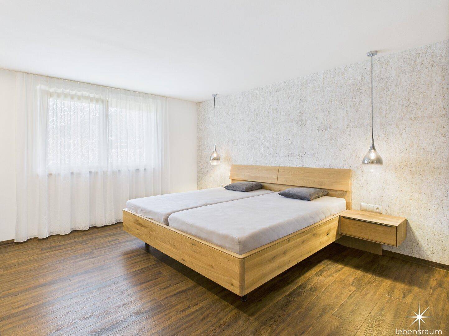 Helles Schlafzimmer mit großem Fenster, Holzboden und minimalistischer Einrichtung.